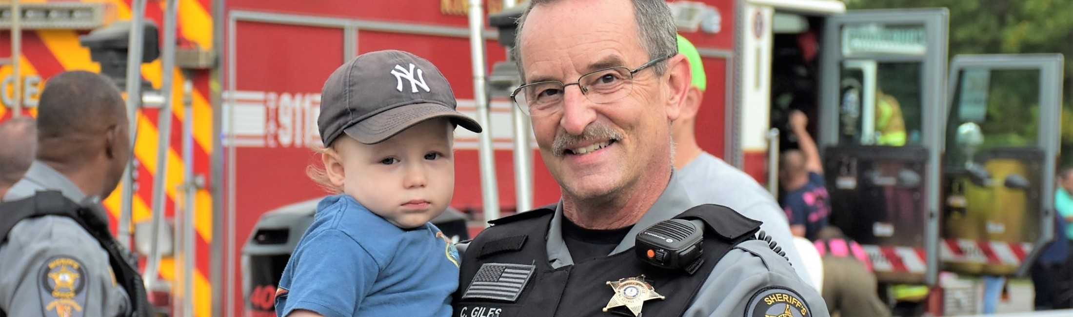 Sheriff holding a child in front of a firetruck