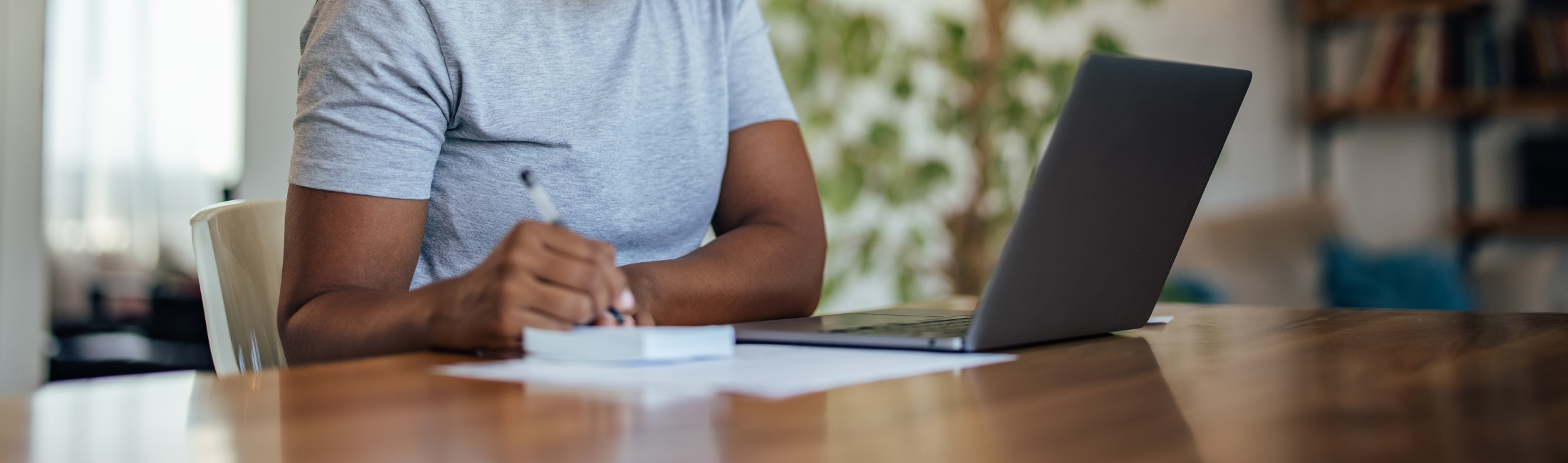 Person sitting at desk writing next to a laptop